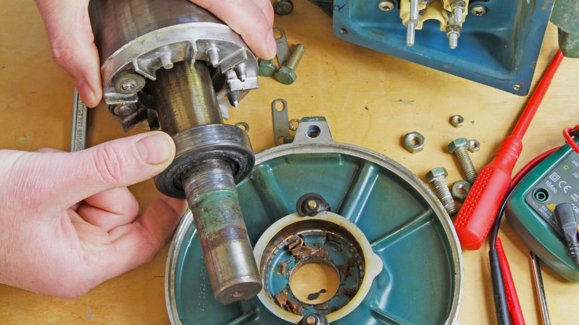 Manos de un técnico reparando el rotor de un motor eléctrico desmontado sobre una mesa de taller.